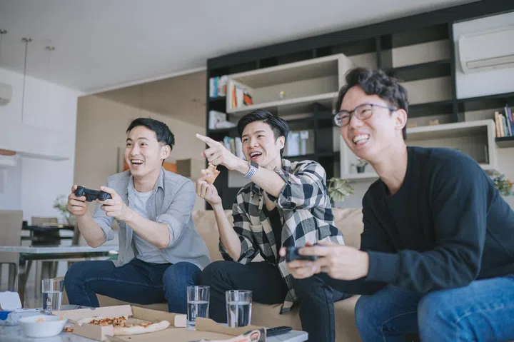 Asian Chinese young man enjoy playing video games with his friend in living room during weekend