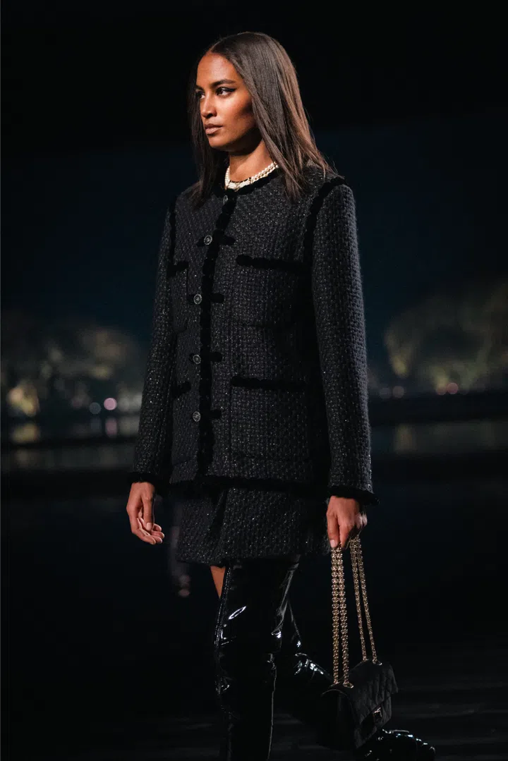 Model in an all-black Chanel outfit with a travel bag