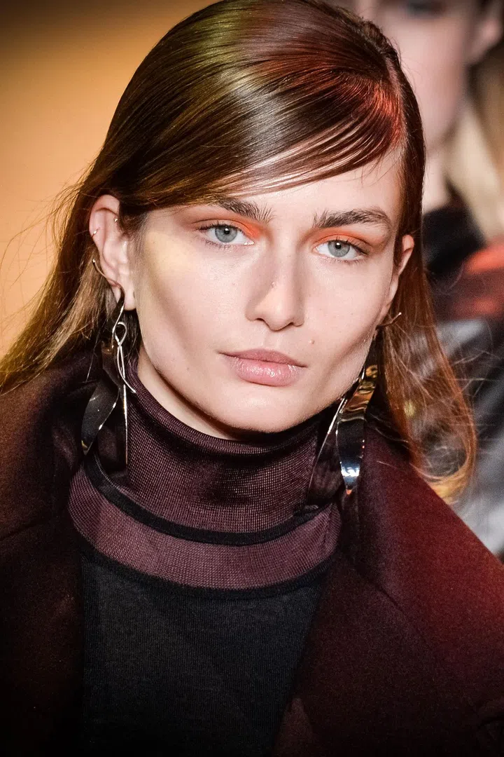 True to form, Mugler's fall collection, with its fiery color palette, leopard prints and thigh-high slits, was not made for wallflowers—and neither were the dominant side parts and flashes of orange on the eyes of some models. Eric Antoniotti, Clarins International Artistic Director, rejected the term 'tribal,' and instead described the streak of earthy orange pigment as "natural art that takes us back to our roots." He mixed a soon-to-come shade of Clarins powder eyeshadow with Blue Orchid Oil on the back of his hand, then swiped the paste across the lids with his fingers. "We want the girls to feel strong," said hairstylist James Pecis, who made side parts, blow-dried the hair smooth with mousse, then draped the front section across the forehead to look like fringe. "Center parts are easy cool, but there's a little bit more strength in the side part. I know that sounds silly, but it does make a difference."