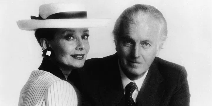 Audrey wears a white and black pin-striped suit with a matching wide-brim hat and oversized earrings for a portrait alongside Givenchy.