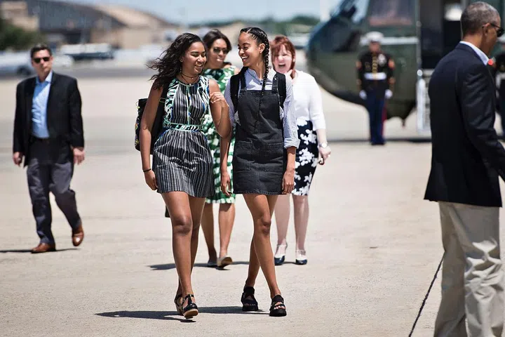 The Obama sisters dressed for summer as they head for New Mexico and California. Sasha wore a printed green dress and her favorite choker, while Malia layered a denim pinafore over a button-down and topped the look off with sleek boxer braids. Photo: Getty