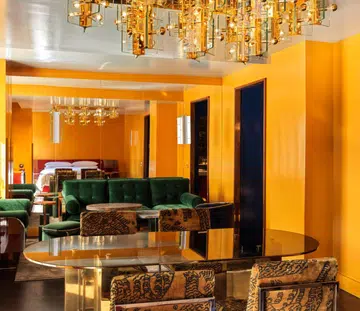 The Manner King Suite with yellow wall, plush green sofa and jacquard dining chairs designed by Hannes Peer