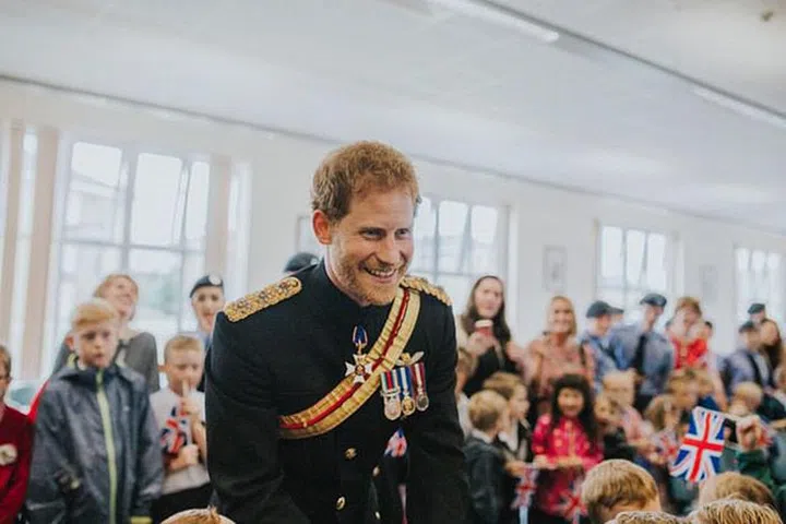 A smiling Harry talking to children while in his military uniform.