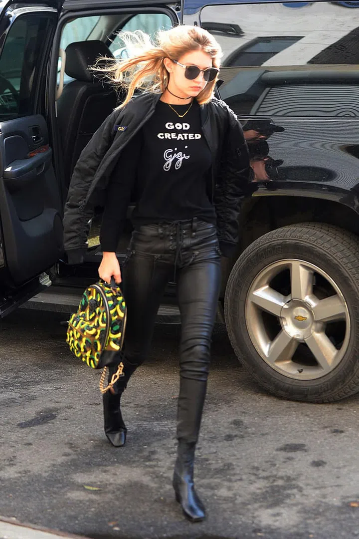 The model sports an edgy all-black ensemble with a custom "Gigi" graphic tee, cool yellow printed bag, and Karen Walker shades. Photo: Getty