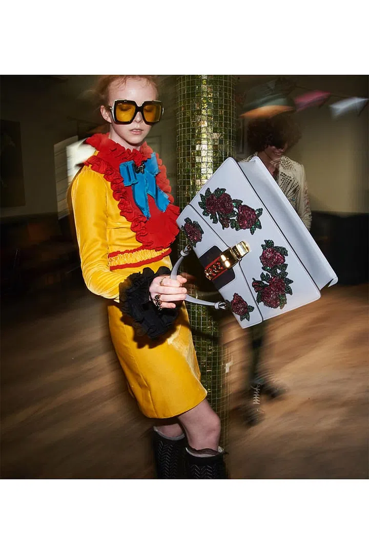 (On her) Silk dress; acetate sunglasses; metal rings; embroidered leather bag; knit socks. (On him) Embroidered and studded leather jacket; denim jeans; leather boots, Gucci.