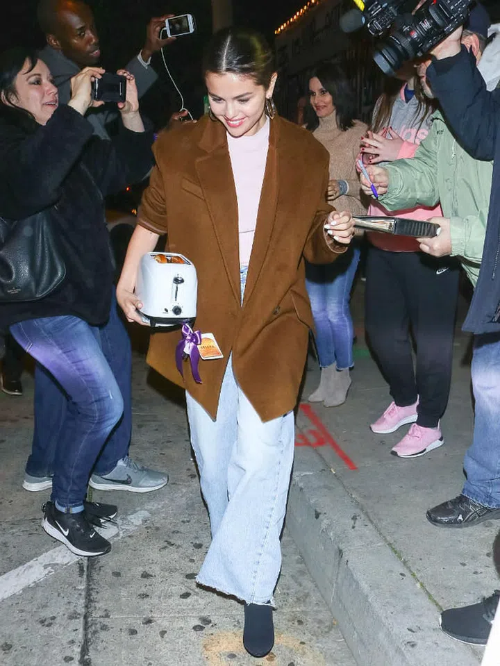 Selena Gomez in a brown trench coat, pale pink top and jeans.

Photo: Getty