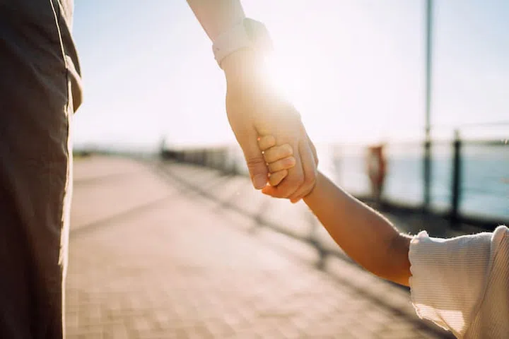Close up of young Asian mother walking hand in hand with her little daughter enjoying family bonding time in a park along the promenade at sunset