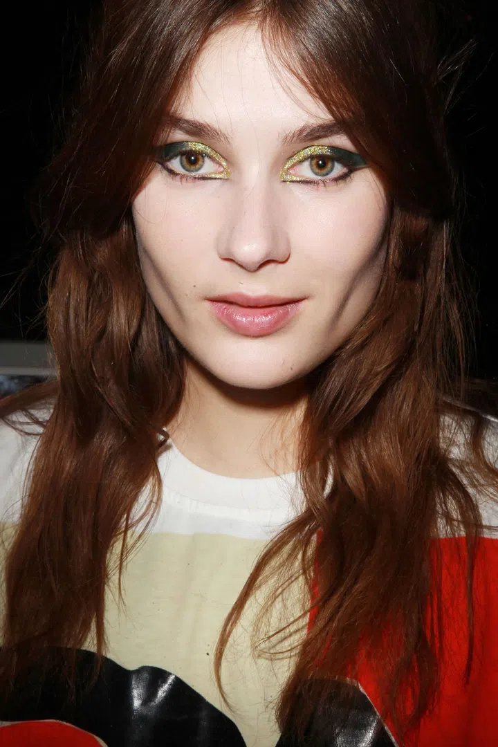 Makeup artist Val Garland cited "Charlotte Rampling in a Helmut Newton photograph" as the inspiration behind the three eye looks she created backstage: one, "a Velvet Underground, rock revolutionary party girl in green [above];" two, romantic pink glitter; and three, "mess-cara," which was more '60s Twiggy than morning after clumpy. To get the final result on the glittery girls to look so precise and pigmented, Garland began by applying cream eye shadow as a base. Next, she went over that with powder shadow to set and intensify it. Then she dipped a liner brush into M.A.C. Mixing Medium, which acts as adhesive, dipped it into glitter and lightly pressed it onto the lid. Black winged liner was added as a final touch to the outside edges for a rock 'n' roll framing.
