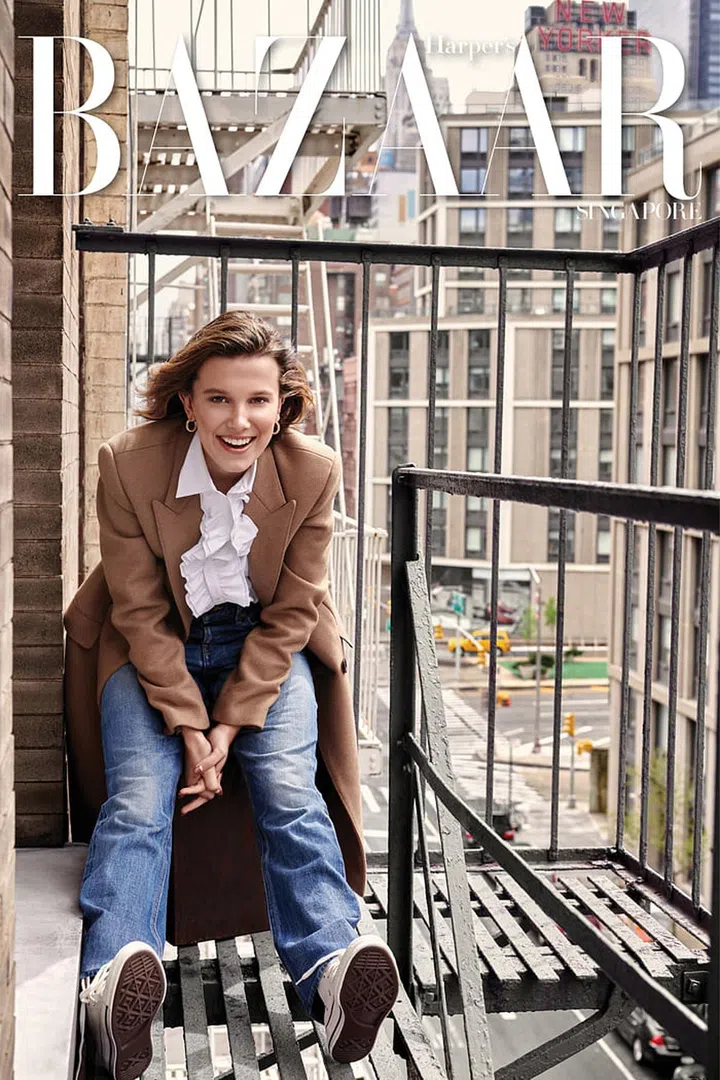 Millie Bobby Brown wears coat; shirt; jeans, CELINE by Hedi Slimane. Gold Clash de Cartier earrings, Cartier. Sneakers, Converse. Photo: Yu Tsai