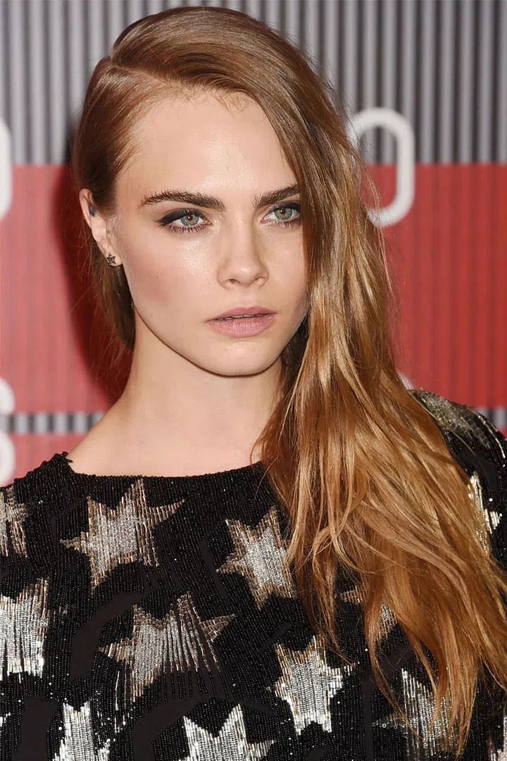Strawberry blonde hair and a deep side part add dimension to Cara Delevingne's long hair.