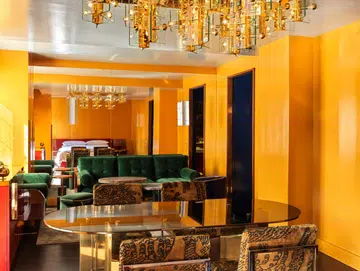 The Manner King Suite with yellow wall, plush green sofa and jacquard dining chairs designed by Hannes Peer