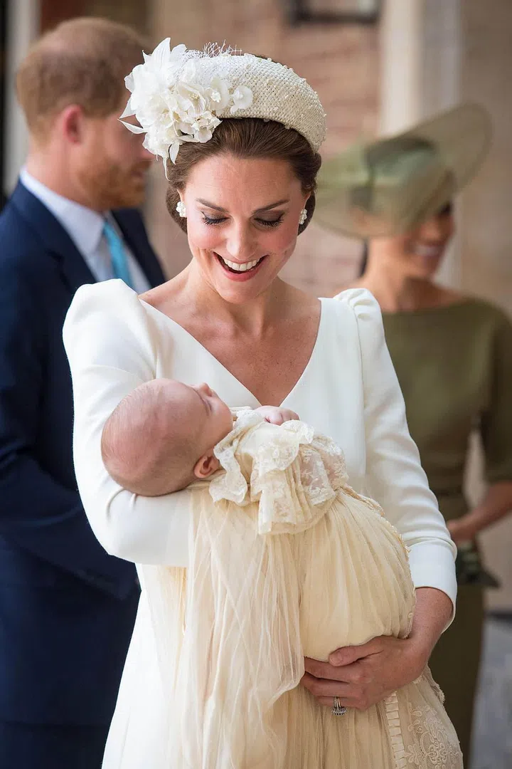 The Duchess of Cambridge, wearing a cream Alexander McQueen dress and Jane Taylor hat, arrives with her youngest son Prince Louis in her arms. Photo: Getty