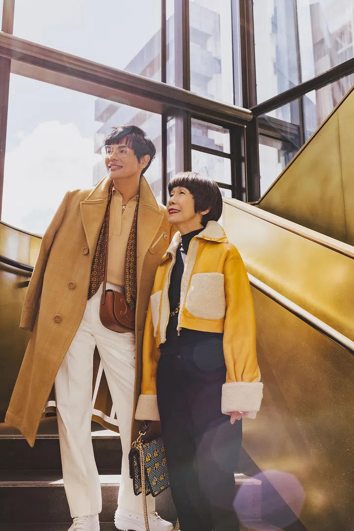 Kenneth Goh, in a Salvatore Ferragamo coat and trousers, a COS top
and Converse shoes worn with
a Prada scarf and a CELINE bag, with his mum Teresa Ooi, rocking a Fendi jacket over a Givenchy top and trousers accessorised with a Miu Miu necklace and a Fendi bag, on the grand staircase in A by Adina Sydney’s 21‐storey sky lobby (Photo: Arvin Prem Kumar)