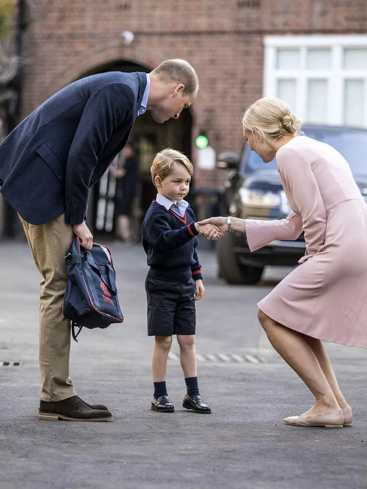 Prince William accompanies Prince George on his first day of school where he meets the headmaster of his school for a handshake.