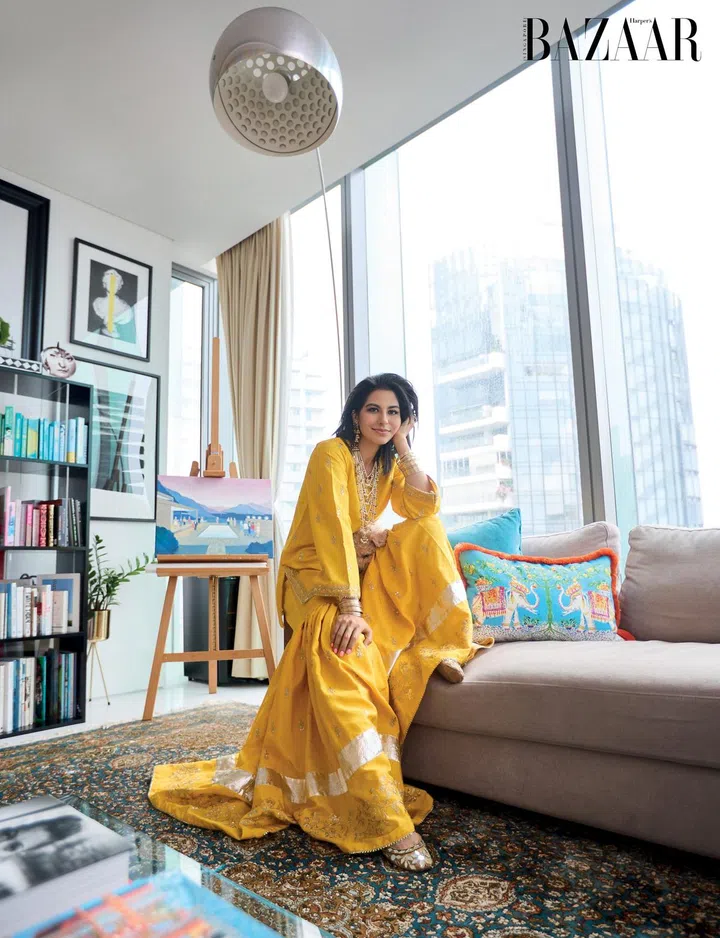 Perched on her living room sofa in front of a painting by her grandfather, Kausar is dressed in traditional wide-legged gharara trousers paired with a kurta, a sat lara necklace and earrings gifted by her in-laws on her first visit to India, together with SunMoonRain bangles, and embroidered traditional shoes from Pakistan.