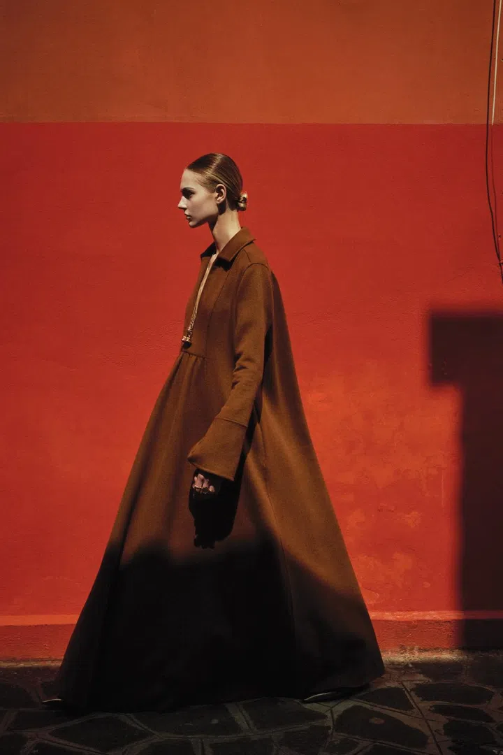 Model wears a brown cashmere long gown from Max Mara Resort 2025 collection, a necklace and sandals shot in Burano island, Venice
