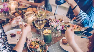 Friends having dinner party at home. It is a feast of food of all color and they are enjoy in every moment of the evening. They are happy and well dressed. Home is decorated with festive string lights and candles. Evening or night.