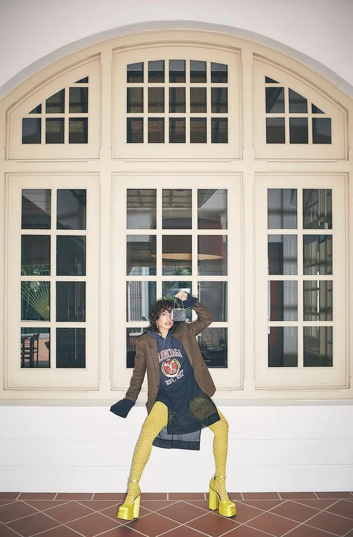 Hoodie, by Balenciaga. Blazer; bag; both by CELINE by Hedi Slimane. Skirt, by H&M. Tights; heels, both by Versace. Ring, by Swarovski. Earrings, by Saint Laurent by Anthony Vaccarello. (Photo: Vernoica Tay)