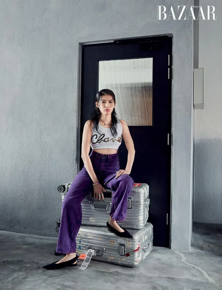 Wong—perched atop her RIMOWA luggage in a Chanel top, Bimba Y Lola trousers and Balenciaga slingbacks teamed with an Omega watch and a Tiffany & Co. ring—in the living area with imperfect walls.