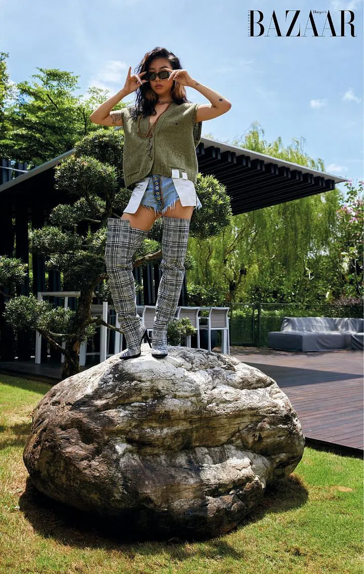 Tan stands tall in the garden in a Gucci vest styled with Salvatore Ferragamo boots and her own denim shorts, sunglasses, necklace and rings.