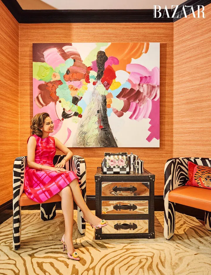 Hunt, in a Carolina Herrera dress and Dolce & Gabbana pumps, relaxes in a corner that has been decorated with a mix of animal prints on the chairs and carpet, and a large abstract artwork.