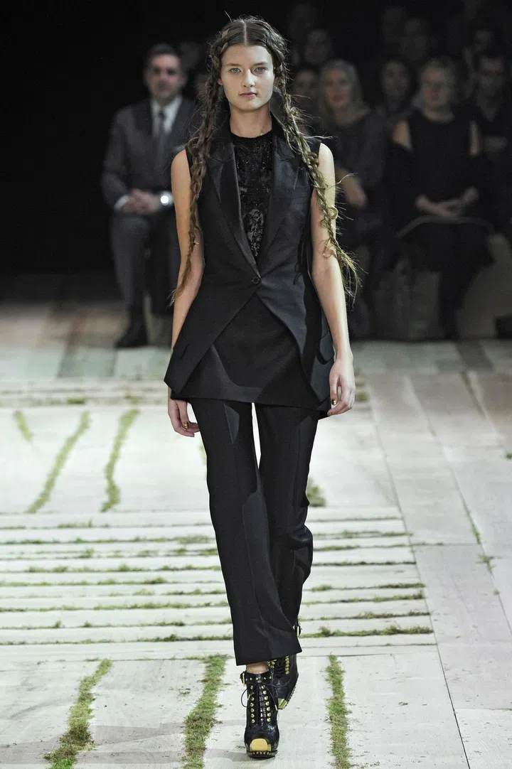 A sleeveless tailored tuxedo jacket with a cutaway front, tonal satin lapels, a single button fastening, two faux flap pockets, a double inverted box pleat at the reverse hem and a vent at centre back in black wool, from the Alexander McQueen Spring/Summer 2011 collection.Credit: Chris Moore/Catwalking.com