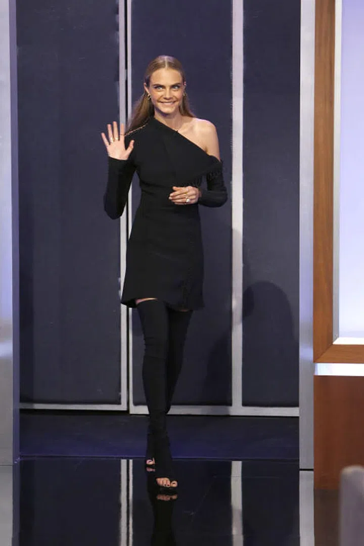 Cara Delevingne appears on Jimmy Kimmel Live in a one-shouldered black dress and over-the-knee boots. Photo: Getty