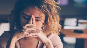Closeup of sad young Asian woman at cafe leaning head on clasped hands and staring into vacancy. Tired freelancer feeling burnout. Stress and bad news concept (Closeup of sad young Asian woman at cafe leaning head on clasped hands and staring into vac