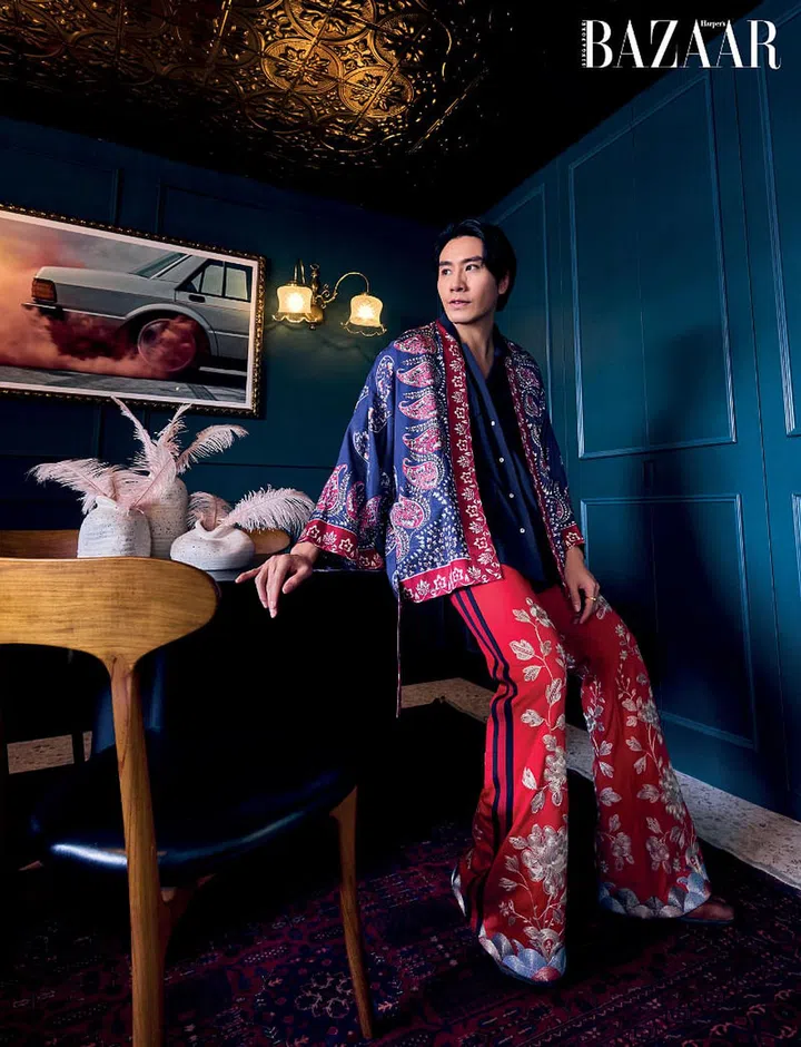 Hong relaxes in his dining room in a Gucci kimono and trousers, shirt from Beyond The Vines, Maison Margiela boots, and Mia Jasmine ring (worn throughout). On the wall behind him are lamps which were formerly from the storied Raffles Hotel.