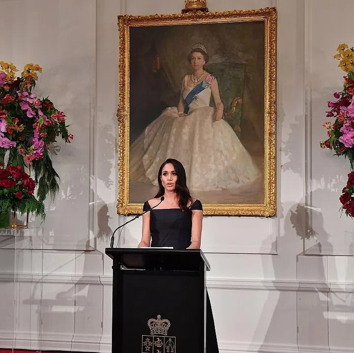 Meghan gives a speech in front of a portrait of Queen Elizabeth II, at Government House in Wellington, New Zealand. Meghan is wearing a dress by Gabriela Hearst. Photo: Getty 