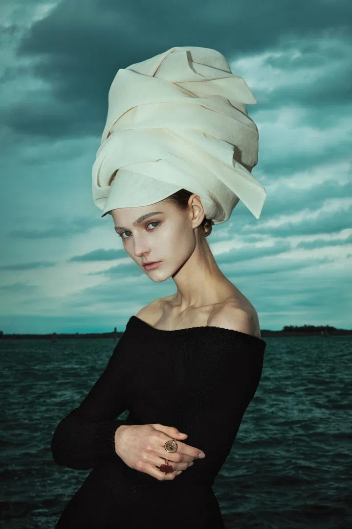 Model wears a black off-shoulder dress from Max Mara Resort 2025 collection and a headgear from Stephen Jones for Max Mara shot in Burano island, Venice