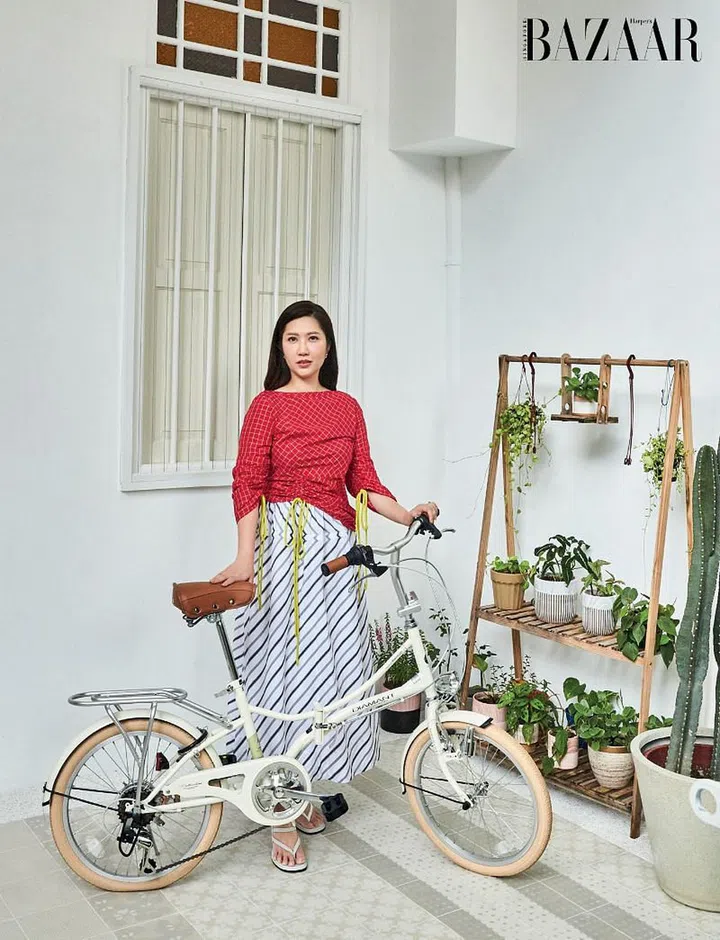 Wong, in a Tory Burch blouse and skirt, Tod’s sandals and her own Chanel earrings, on her front porch with a Diamant bicycle.
