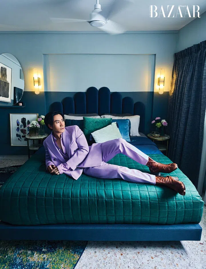 Hong wears a BOSS pantsuit and boots from Maison Margiela as he lounges on his bed with its scalloped headboard which was a deliberate choice, along with the organically-shaped mirror, to contrast with the square
layout of the bedroom.