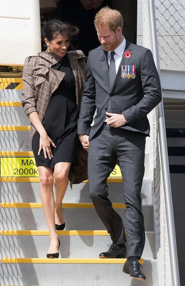 Harry and Meghan arrive into Wellington airport in New Zealand. Meghan is wearing an affordable ASOS maternity dress, with a Karen Walker Banks plaid trench, and her favorite Sarah Flint pumps. Photo: Getty 