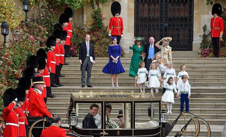 The bridal party looks on as the bride and groom depart in a carriage.