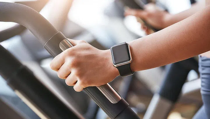 Smart technologies. Close-up photo of smart watch on woman hand holding the handle of cardio machine in gym. Fitness and sport concept.