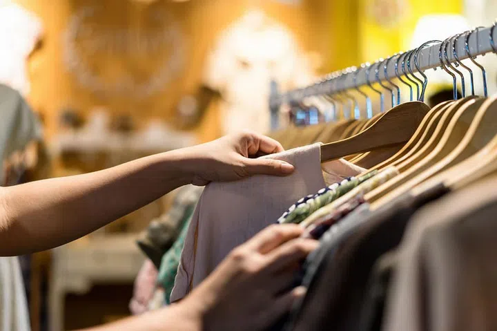 Close up of woman hand choosing thrift young and discount t-shirt clothes in store, searching or buying cheap cotton shirt on rack hanger at flea market , stall shopping apparel fashion concept