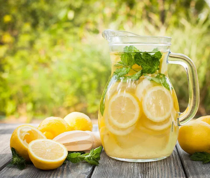 Preparation of the lemonade drink. Lemonade in the jug and lemons with mint on the table outdoor