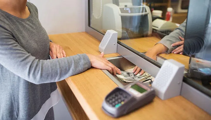 people, withdrawal, saving and finance concept - clerk giving cash money to customer at bank office or currency exchanger