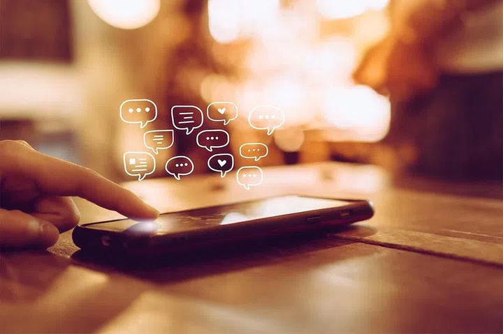 Women hand using smartphone typing, chatting conversation in chat box icons pop up. Social media maketing technology concept.Vintage soft color tone background.