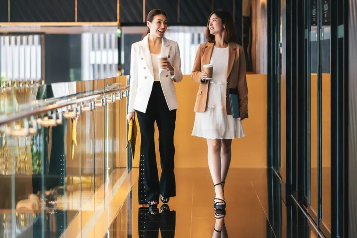 Two asian businesswomen walking and talking during coffee break in modern office or coworking space, coffee break, relaxing and talking after working time, business and people partnership concept