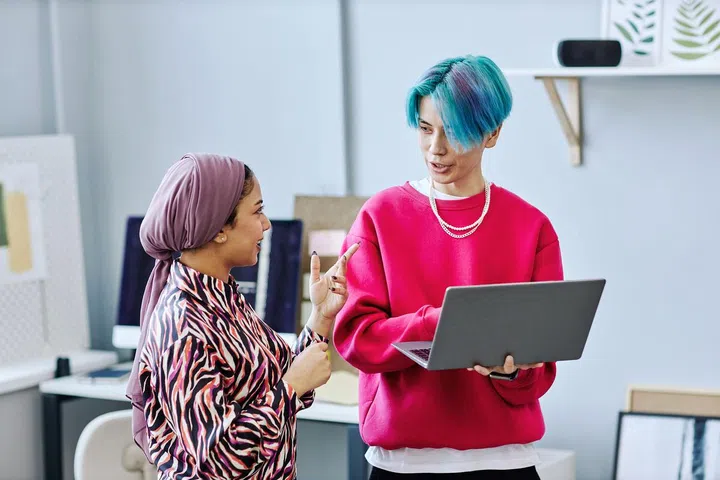 Waist up portrait of creative gen Z team discussing project while standing in office and holding laptop