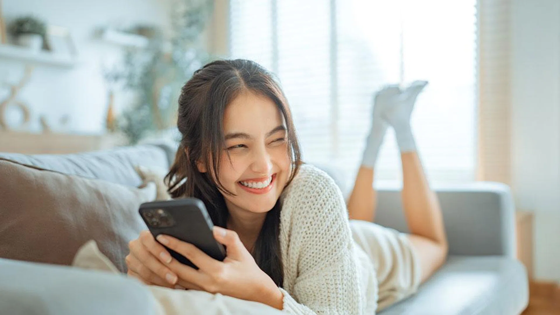 girl lying on couch using phone smiling | best online shopping sites for beauty products