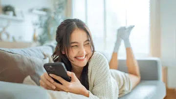 girl lying on couch using phone smiling | best online shopping sites for beauty products