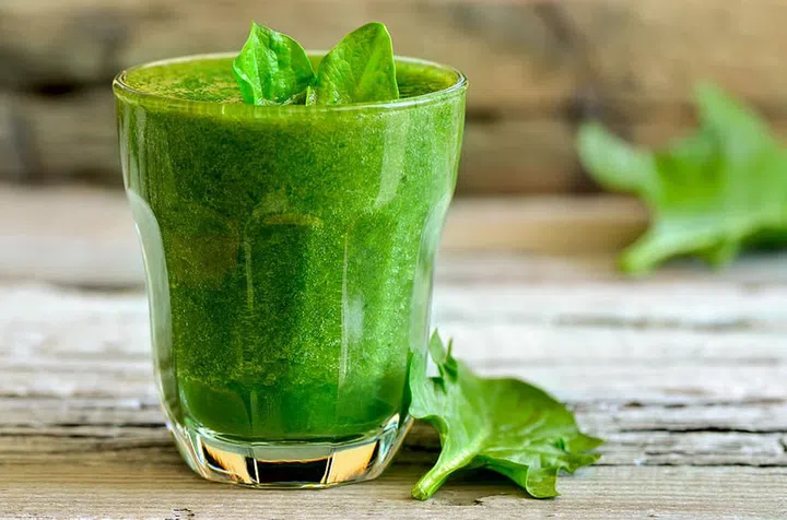 Green spinach smoothie in a glass with fresh leaves