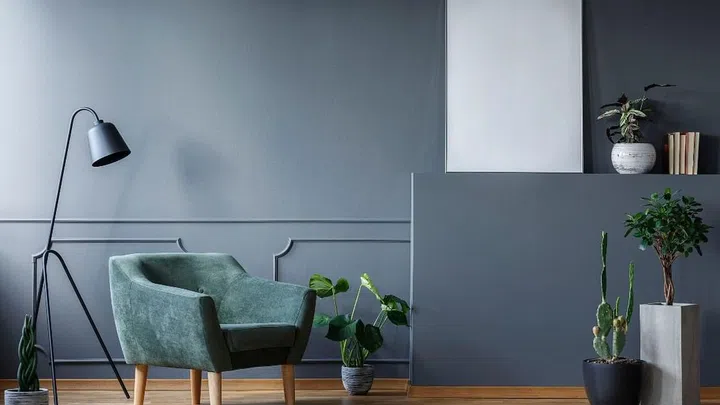 Black lamp next to green armchair in living room interior with plants and mockup of poster