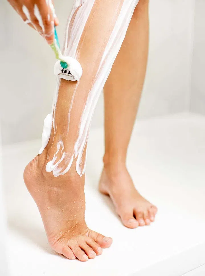 Woman shaving her legs with razor and foam in the shower cabin