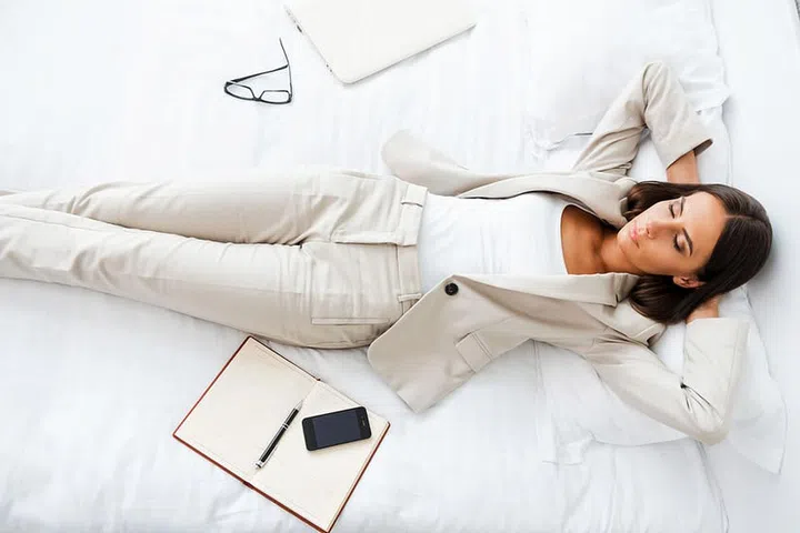 Taking rest hard working day. Top view of beautiful young businesswoman in suit holding hands behind head and keeping while lying in bed at the hotel room
