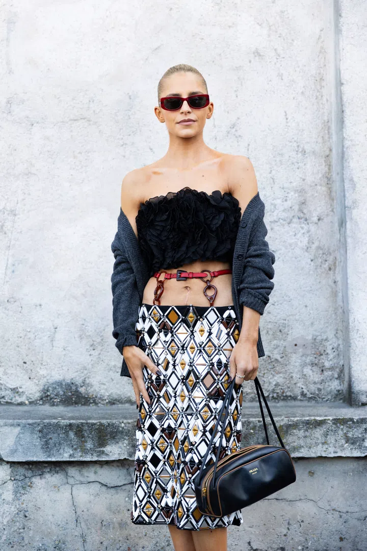 MILAN, ITALY - FEBRUARY 27: Caro Daur wears red sunglasses, a red belt, a black shoulder-less crop top, a black and silver low waist midi skirt and a black leather bag outside Prada show during the Milan Fashion Week Womenswear Fall/Winter 2025/2026 on February 27, 2025 in Milan, Italy. (Photo by Valentina Frugiuele/Getty Images)
