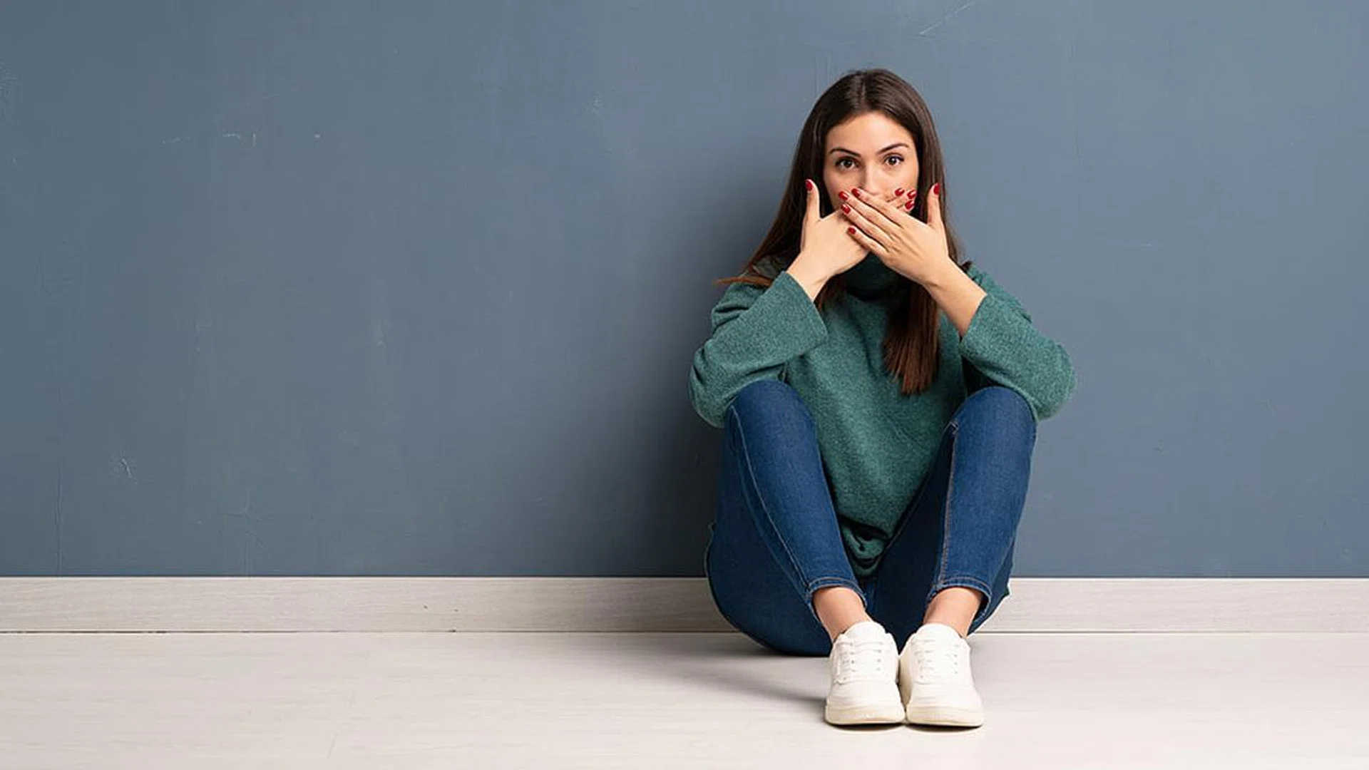 Young woman sitting on the floor covering mouth with hands for saying something inappropriate